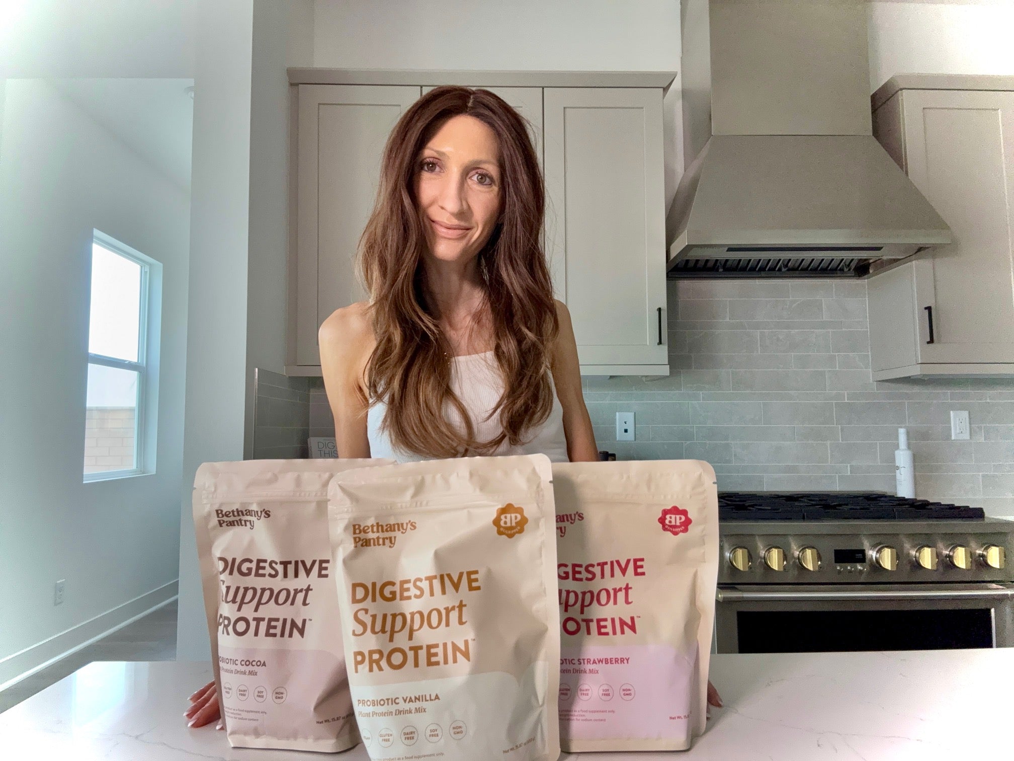 Bethany Cameron lilsipper holding bags of digestive support protein in a kitchen